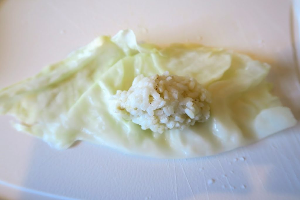 A ball of rice on top of a semi-circle of cabbage about half an inch away from the cut side