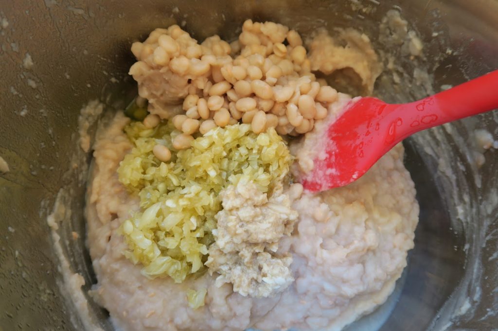 Combining the cooked onions, mashed garlic and reserved beans with the mashed beans