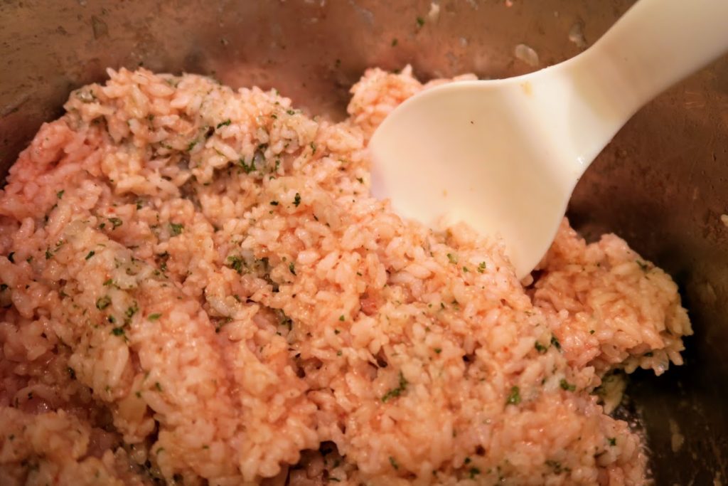 Cooked rice with a reddish hue from the tomato juice stirred with parsley being mixed in