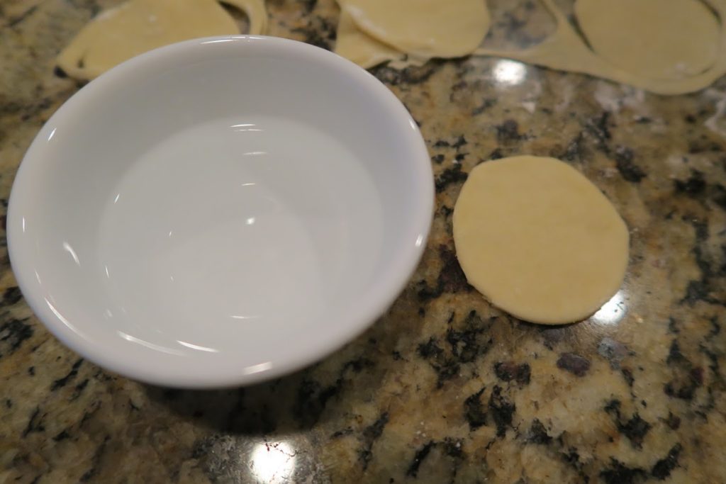 A small bowl of water next to a circle of dough