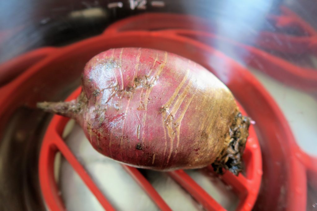 A giant beet in the Instant Pot on a silicone trivet